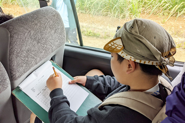バスの中で調査表に記入している生徒の写真