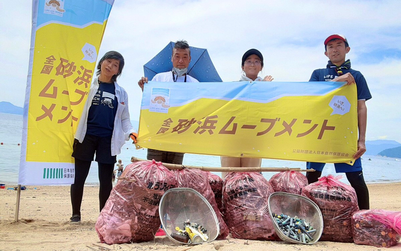 砂浜ムーブメント横断幕とゴミ袋の集合写真