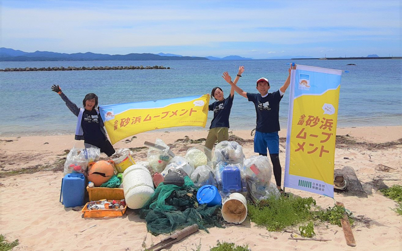 NACSJスタッフが砂浜で横断幕を掲げている写真