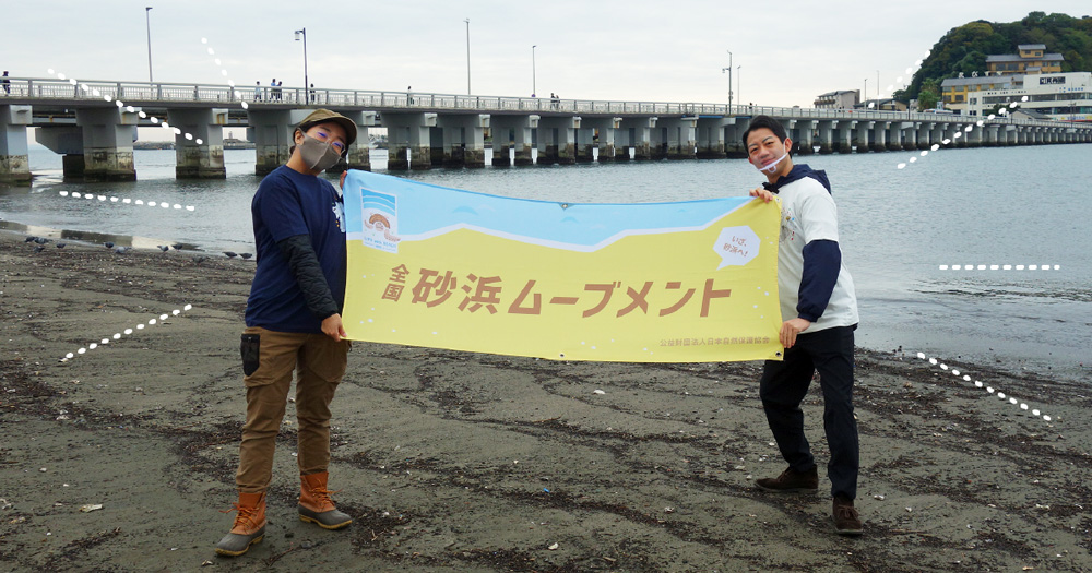 砂浜ムーブメントの横断幕を持つ中村壱太郎さんの写真