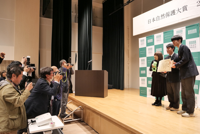 大勢の記者にカメラを向けられる受賞者の写真