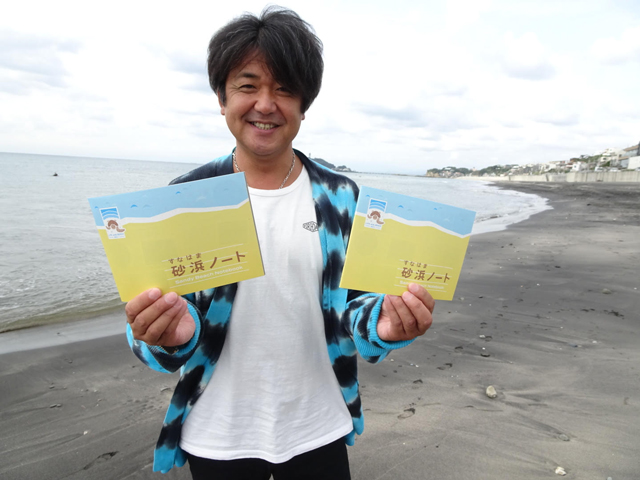 砂浜ノートを持つ鍵井靖章さんの写真