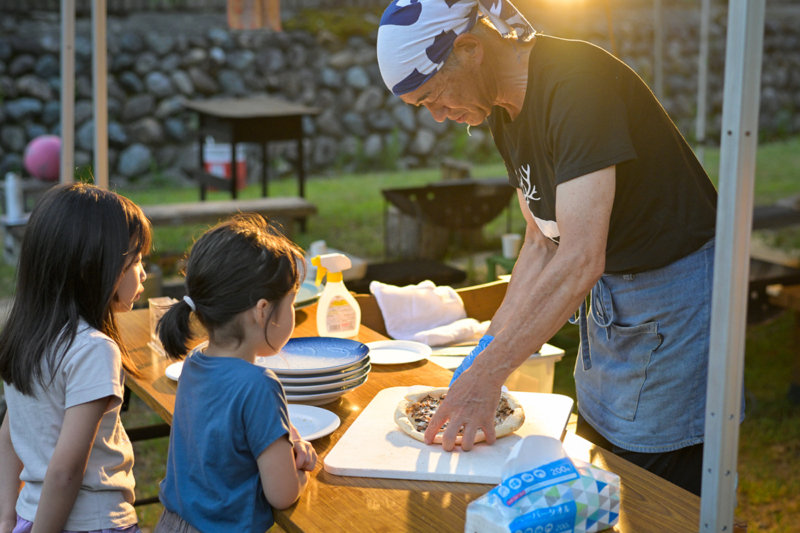 ピザを焼く大人とそれを見守る子どもの写真