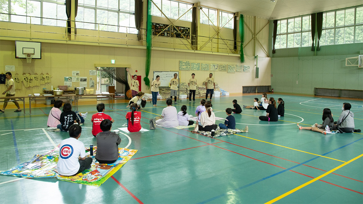 体育館で説明を聞く人々の写真