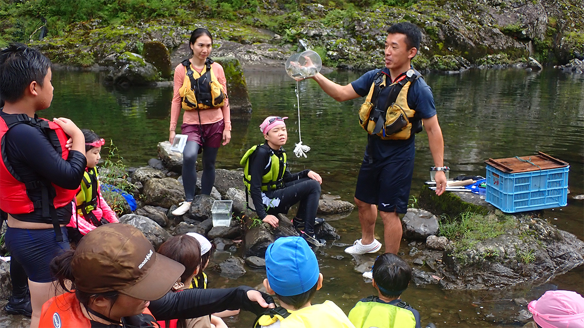 川縁で説明を聞く子どもたちの写真