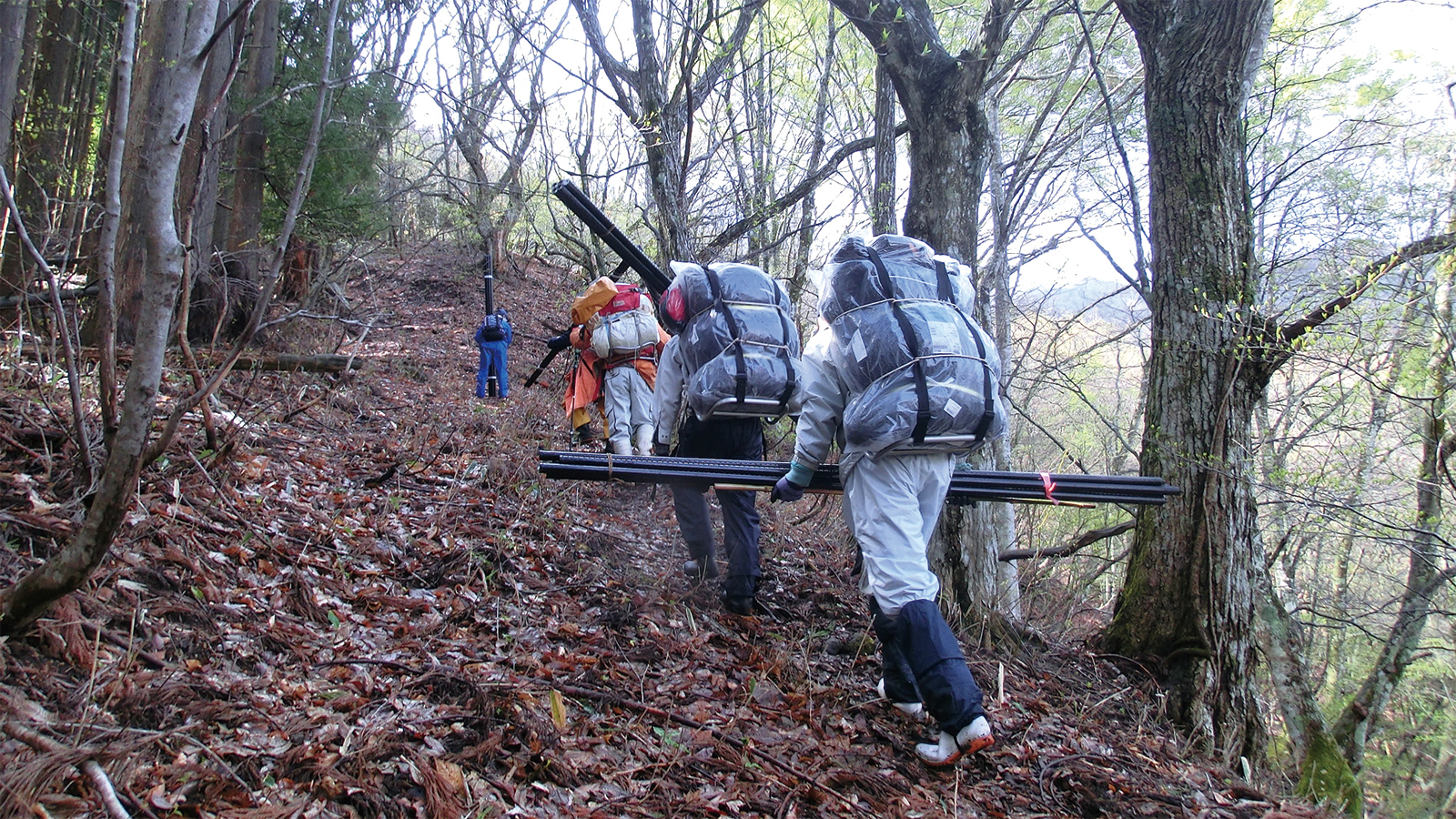 資材を背負って山道を歩く人の写真